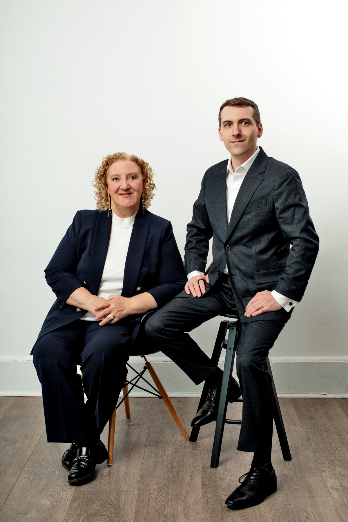 Connie & Andrew dressed in suits and sitting on stools.